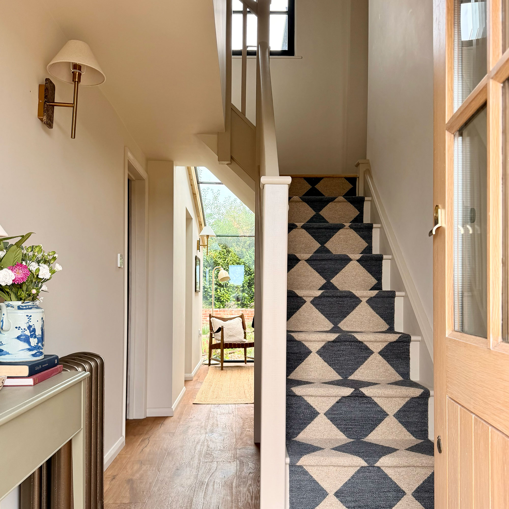 Entrance hall with neutral walls, wooden flooring and staircase with monochrome chequered runner