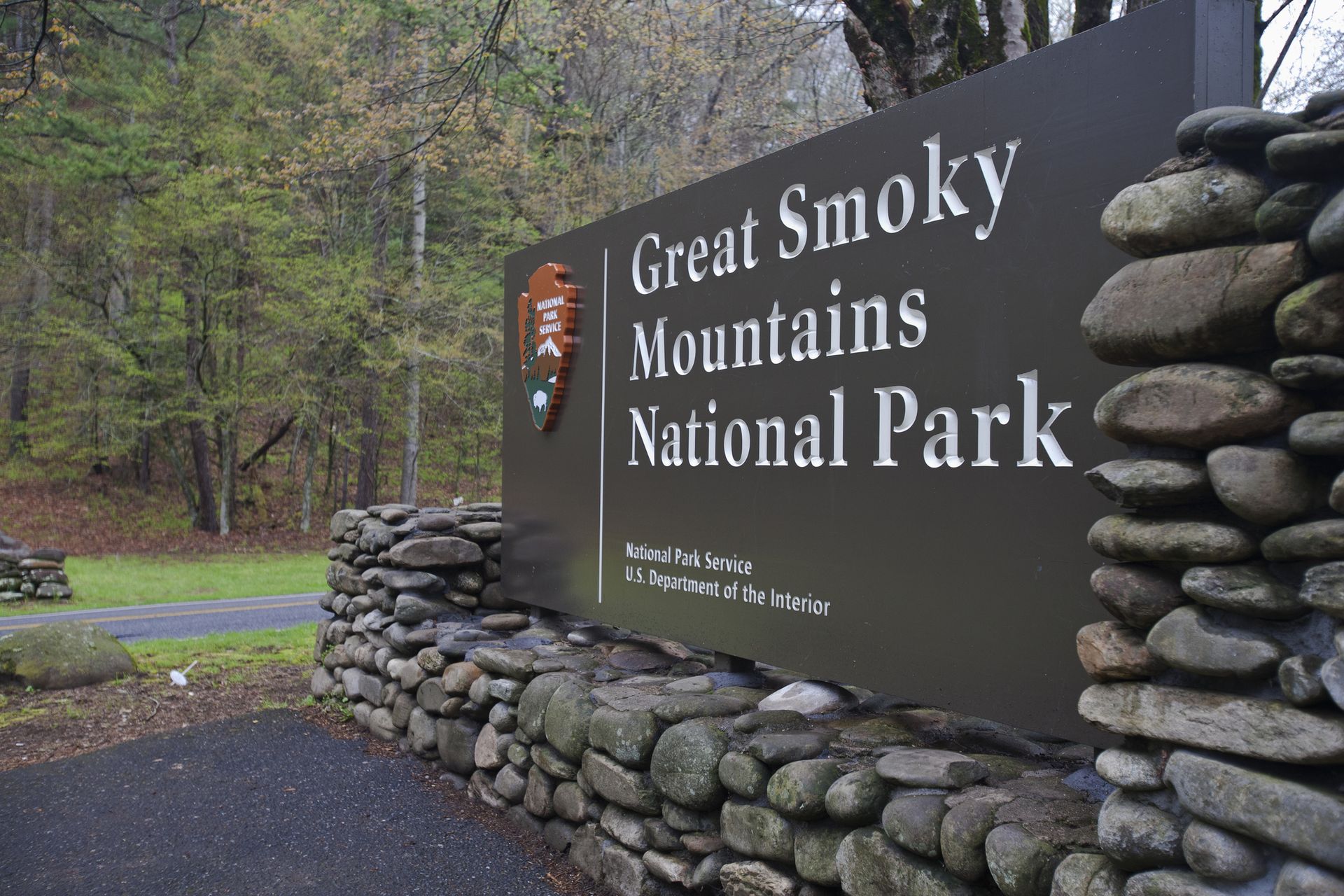 Rocky sign of the Great Smoky Mountains National Park with trees and a road