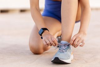 A close up of a woman kneeling while tying her trainers up.