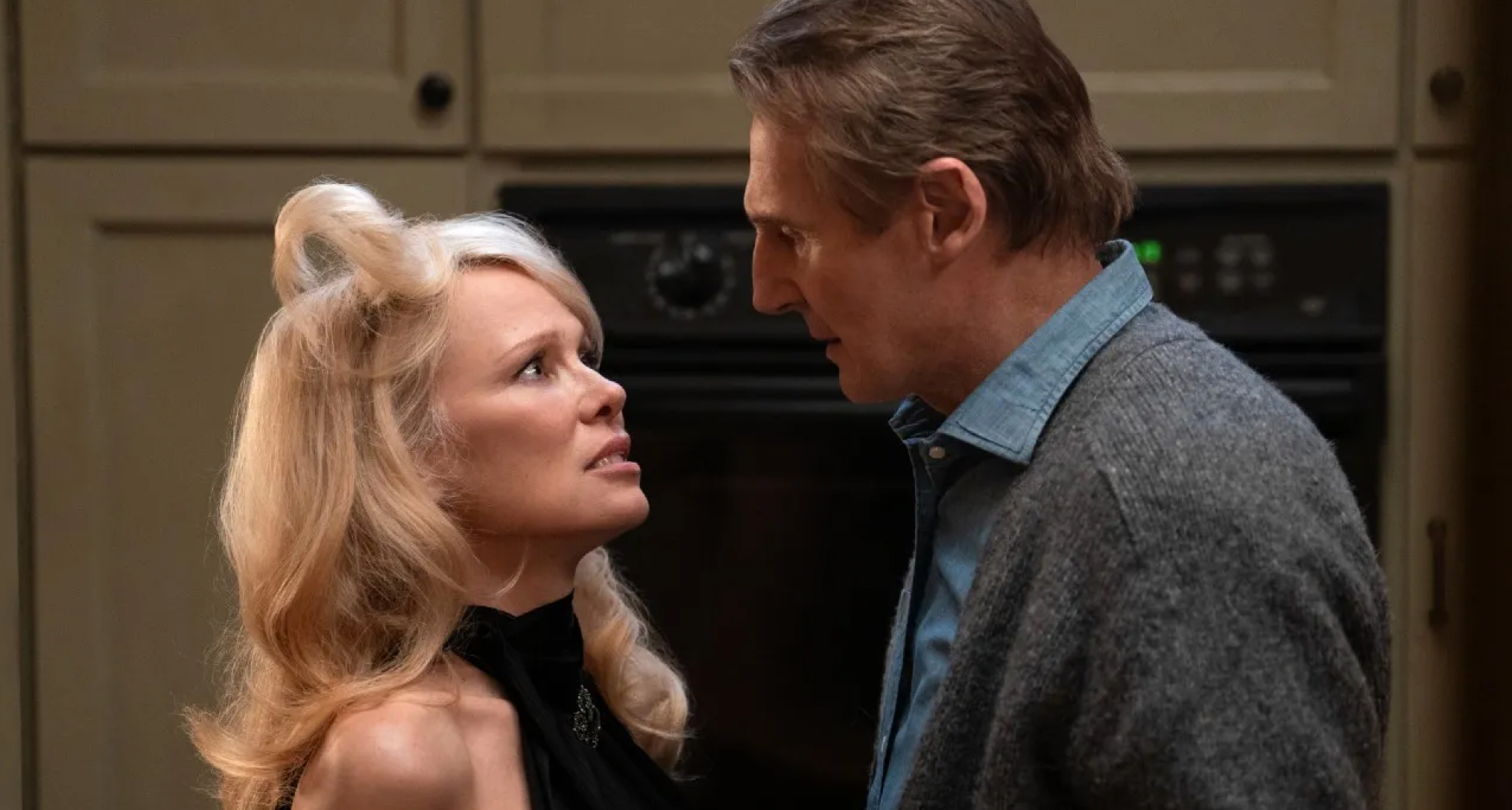 pamela anderson with her hair flipped up and liam neeson stare at each other in a kitchen in a still from the naked gun