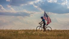 Picture of a cyclist waving american flag in an open field in Oklahoma against a dramatic cloudy sky on Independence Day.
