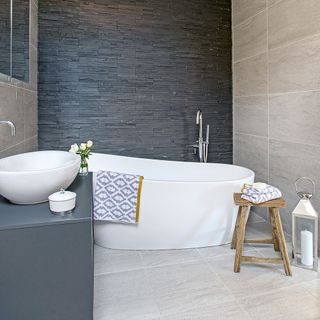 Bathroom with oval bathtub, grey stone wall and beige tiles on wall and floor