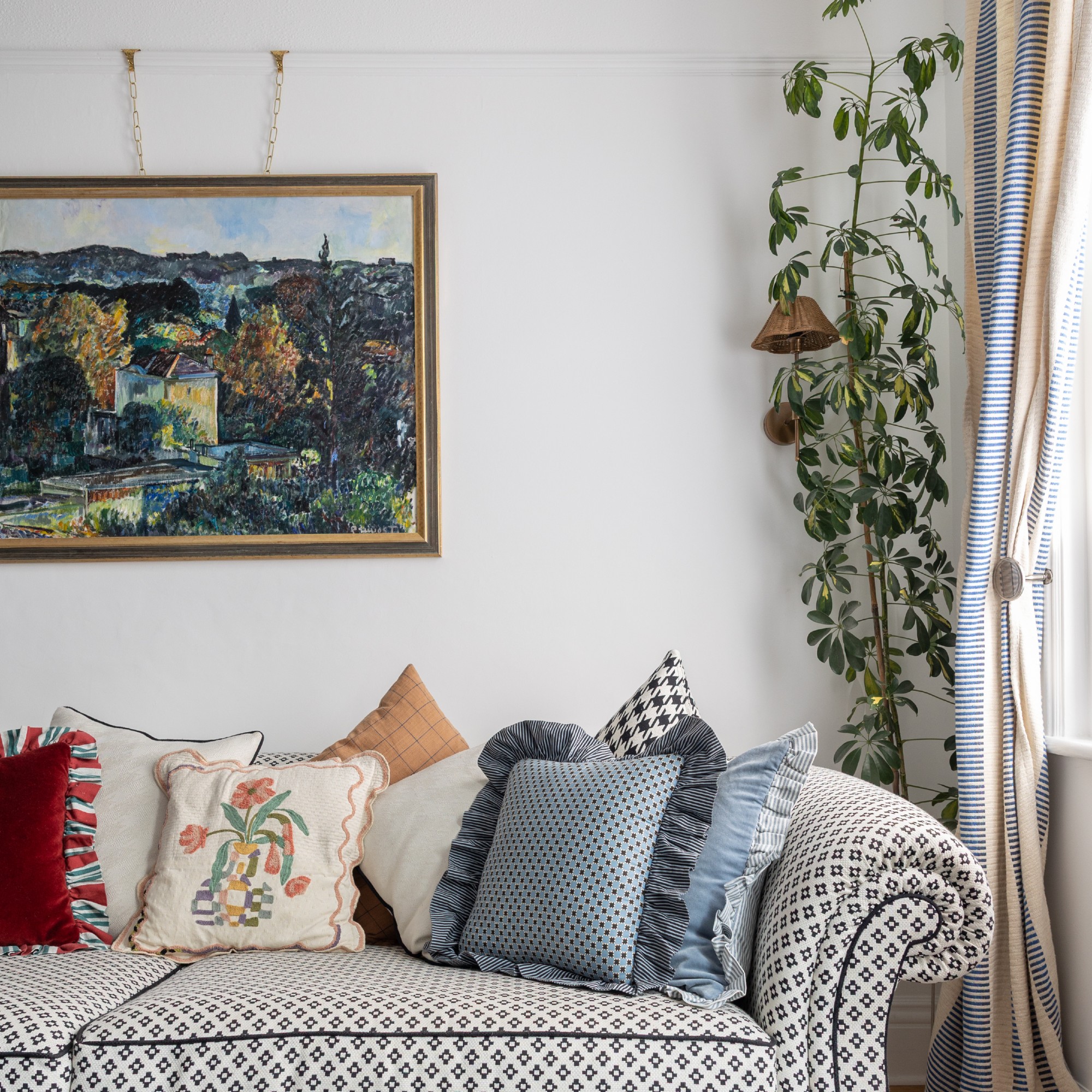 A living room with a patterned sofa and a painting hanging above it on a picture rail
