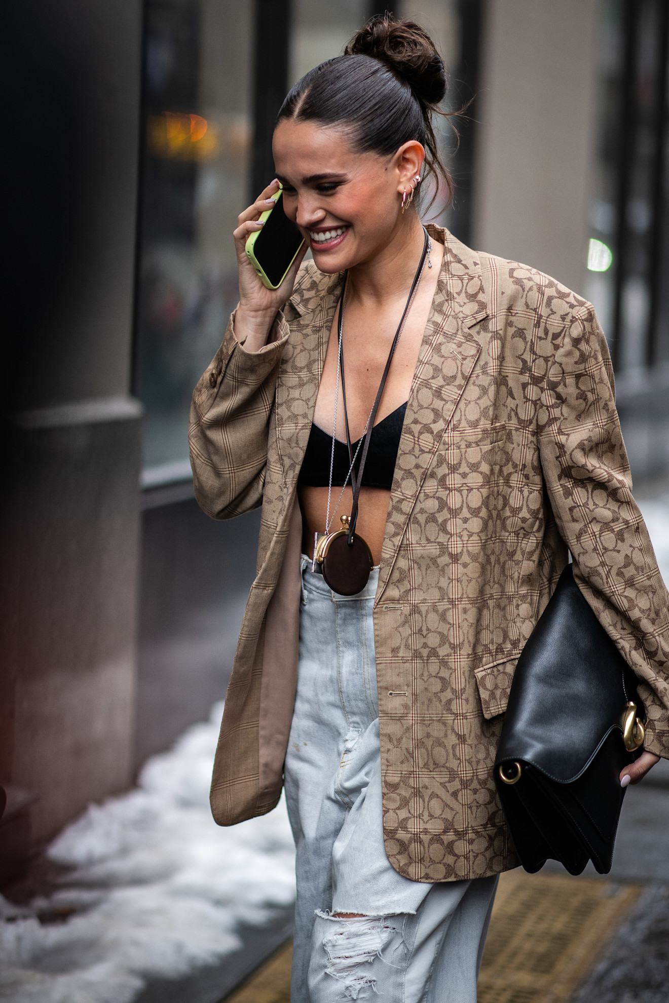 a woman in a tan Coach jacket and jeans with a dark brown bun