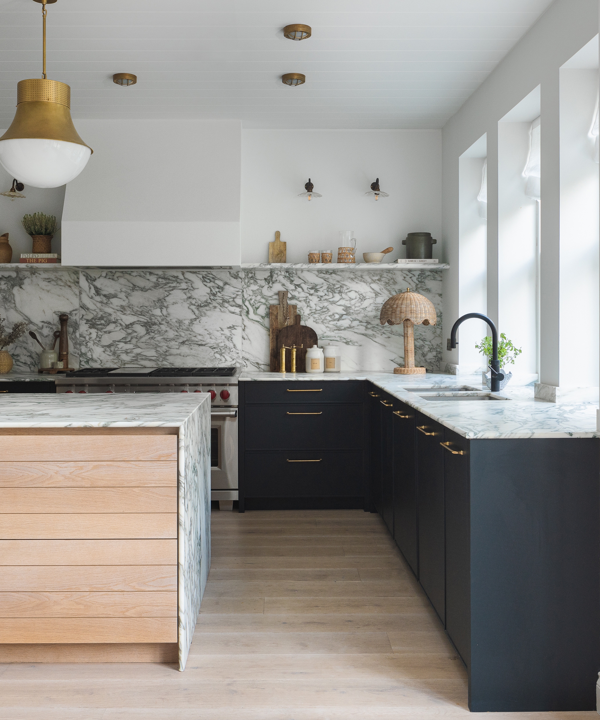 A navy and white kitchen with marble countertops, a wood island, and layered lighting