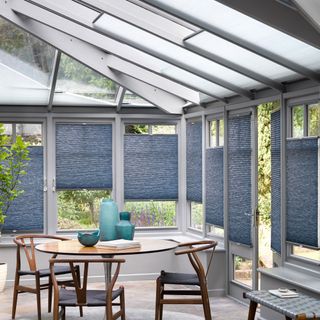 A conservatory with blue blinds and a wooden dining table