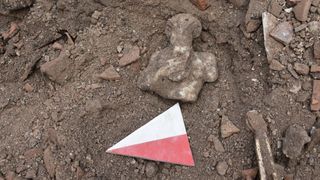 We see the dirt- and rock-filled earth at an archaeological site. The Pan statue is covered with dirt and on its back.