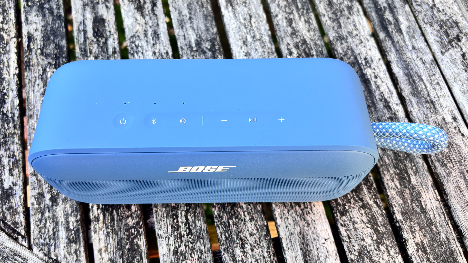 Bose SoundLink Plus wireless speaker on wooden garden table top down view showing top of speaker and controls