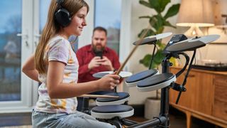 Girl in white t-shirt plays an electronic drum set in front of her dad