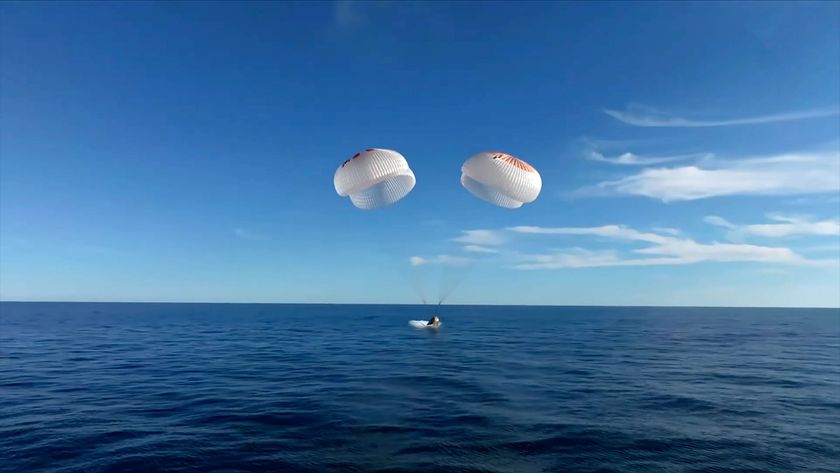 a space capsule under four white and orange main parachutes splashes down in the Gulf of Mexico.