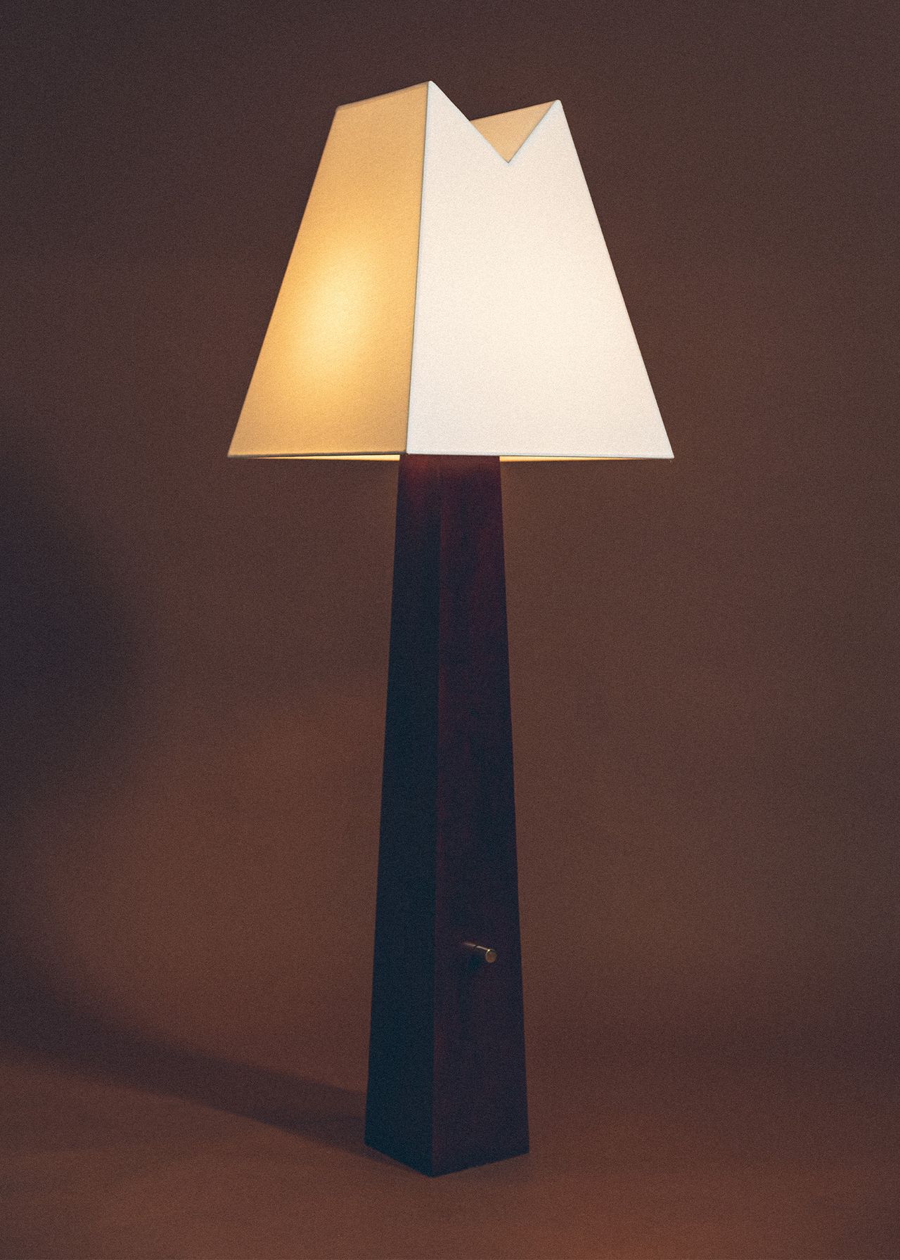 A standing lamp with minimalist, geometric lines features a burgundy base and a light yellow shade.