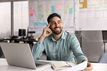 Happy professional man sits in workplace desk with laptop, organizer and papers.
