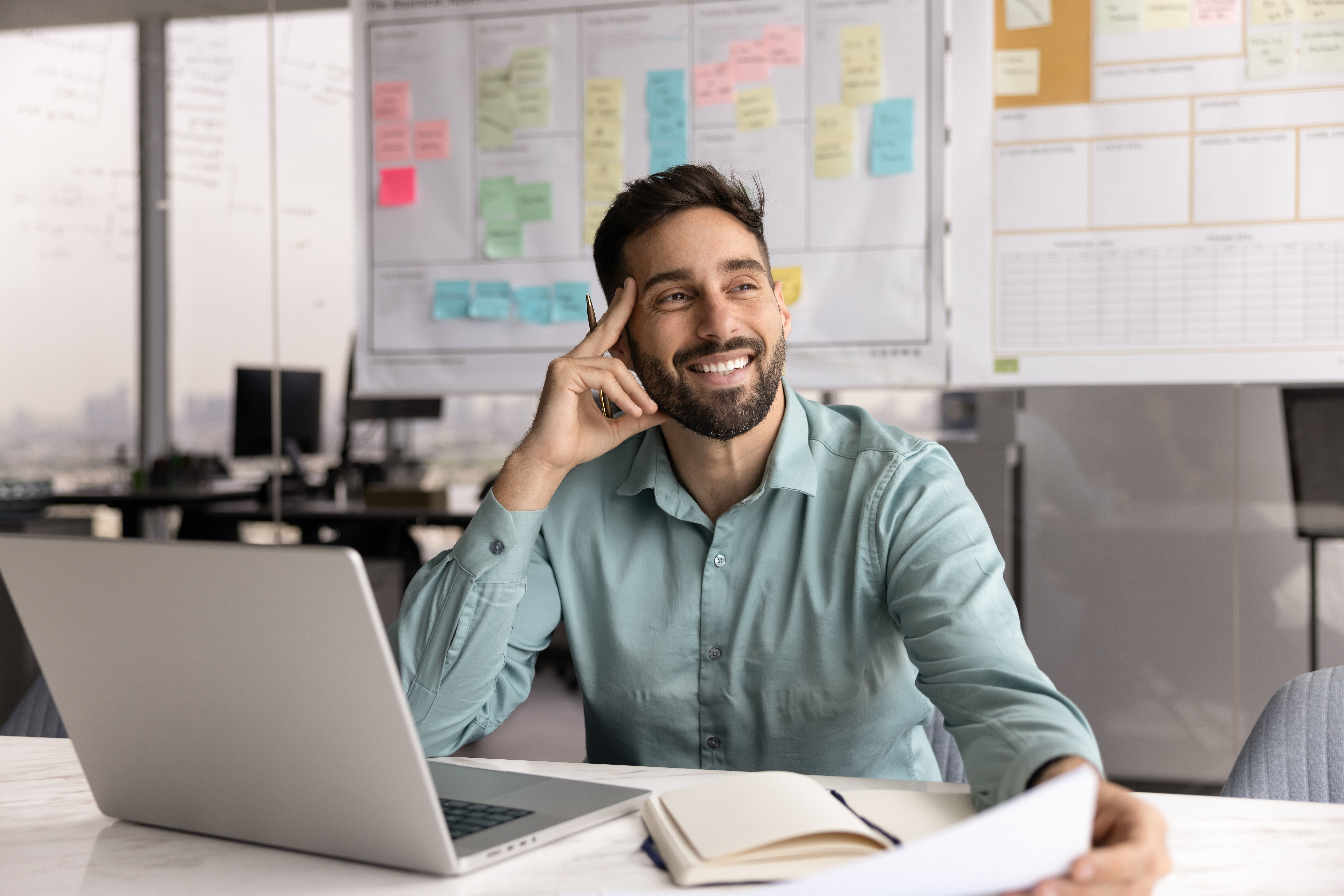 Happy professional man sits in workplace desk with laptop, organizer and papers.