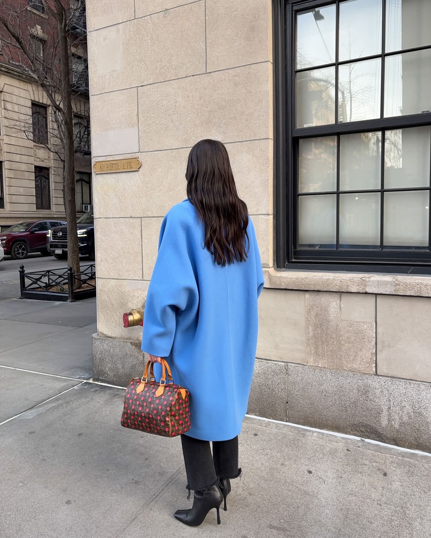 Influencer @inchargeofoutfits stands outside wearing a blue coat with a Louise Vuitton Speedy bag.