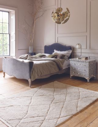 bedroom with blue/grey upholstered bed, wooden floors, patterned rug, leaf shaped pendant light