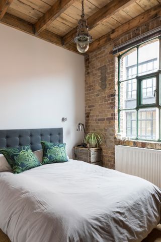 How to use exposed brick: exposed brick on window wall in industrial-style bedroom with exposed ceiling beams