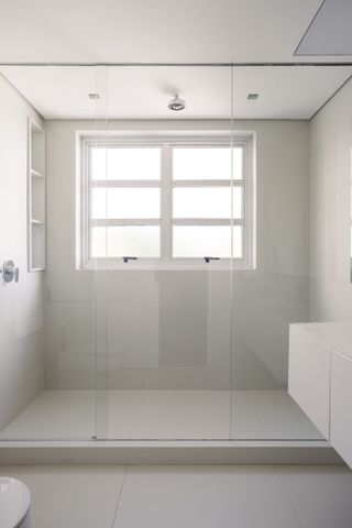 An all white bathroom with transparent shower partitions