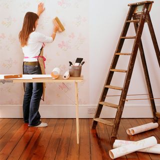 women sticking rose colour wall paper with ladder
