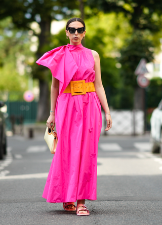 Gabriella Berdugo wears eyecat sunglasses form Stella Mccartney, a Fuchsia neon pink nylon long turtleneck dress with couture pads shoulder pleated / gathered details, an orange maxi belt from Natan, neon pink sliders bejeweled sandals from Roger Vivier, a vintage vinyl beige long bag with embossed monograms from Louis Vuitton, on August 02, 2021 in Paris, France