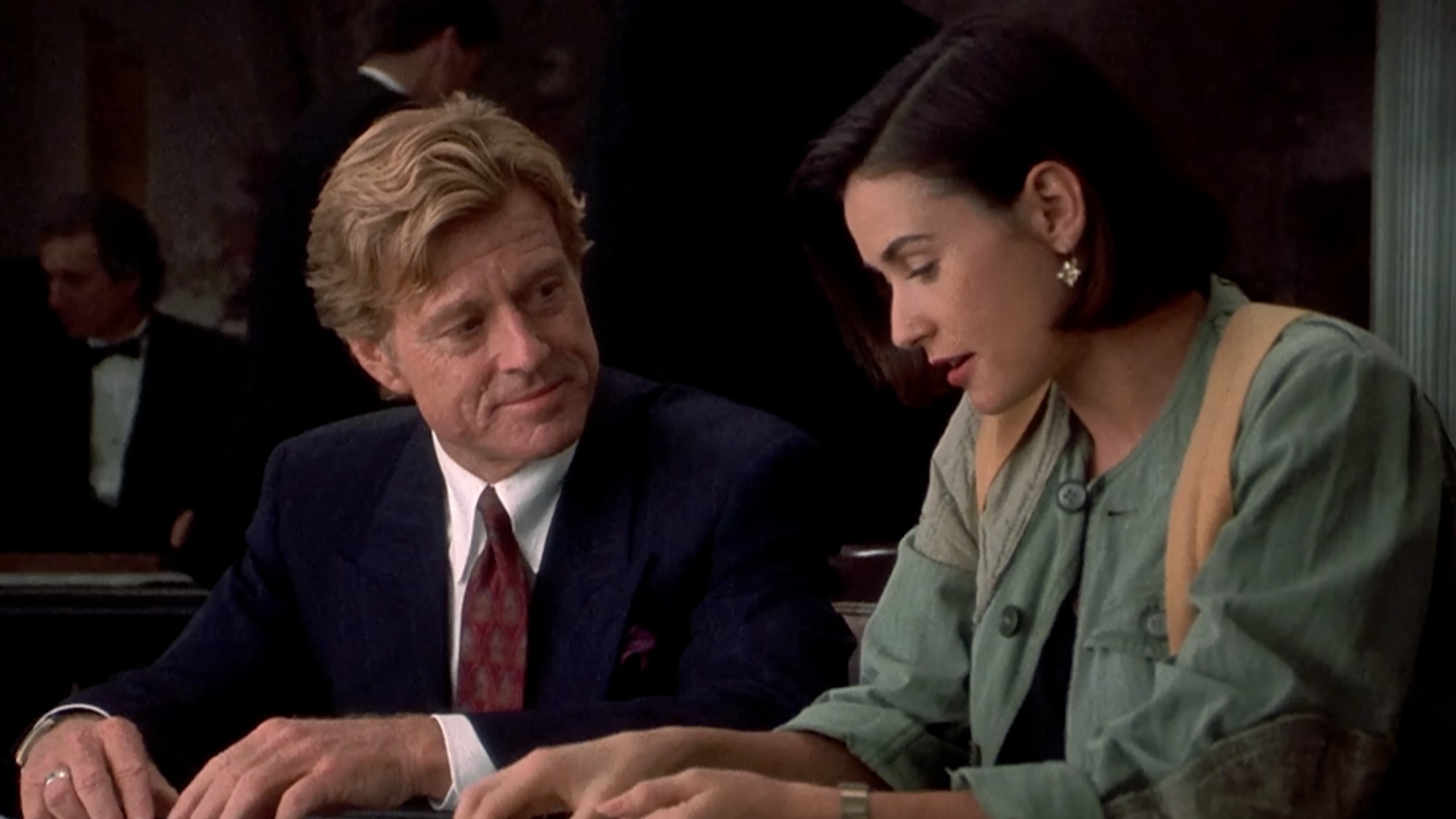Robert Redford in a suit, looking over at Demi Moore in a green jacket in Indecent Proposal