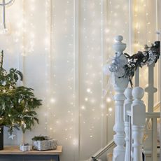 Curtain string lights along way leading up staircase beside Christmas tree