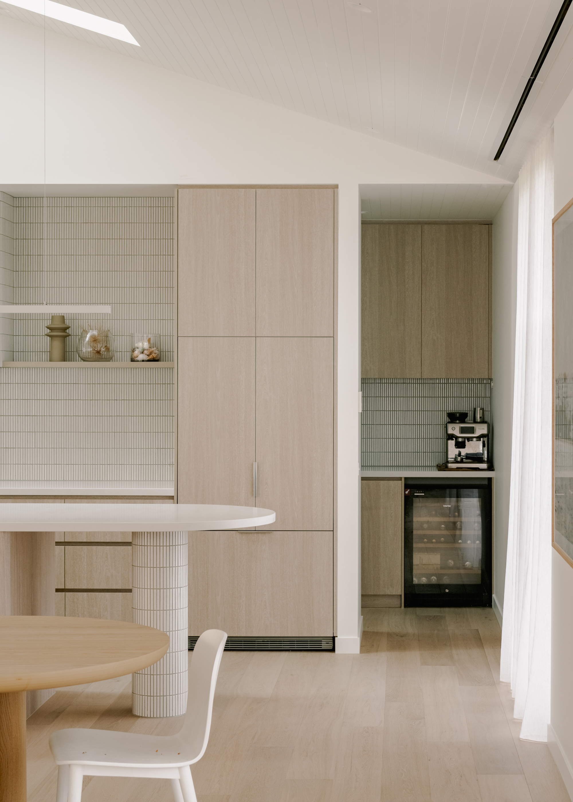A pared-back minimalistic kitchen and dining space with light wood and white marble accents