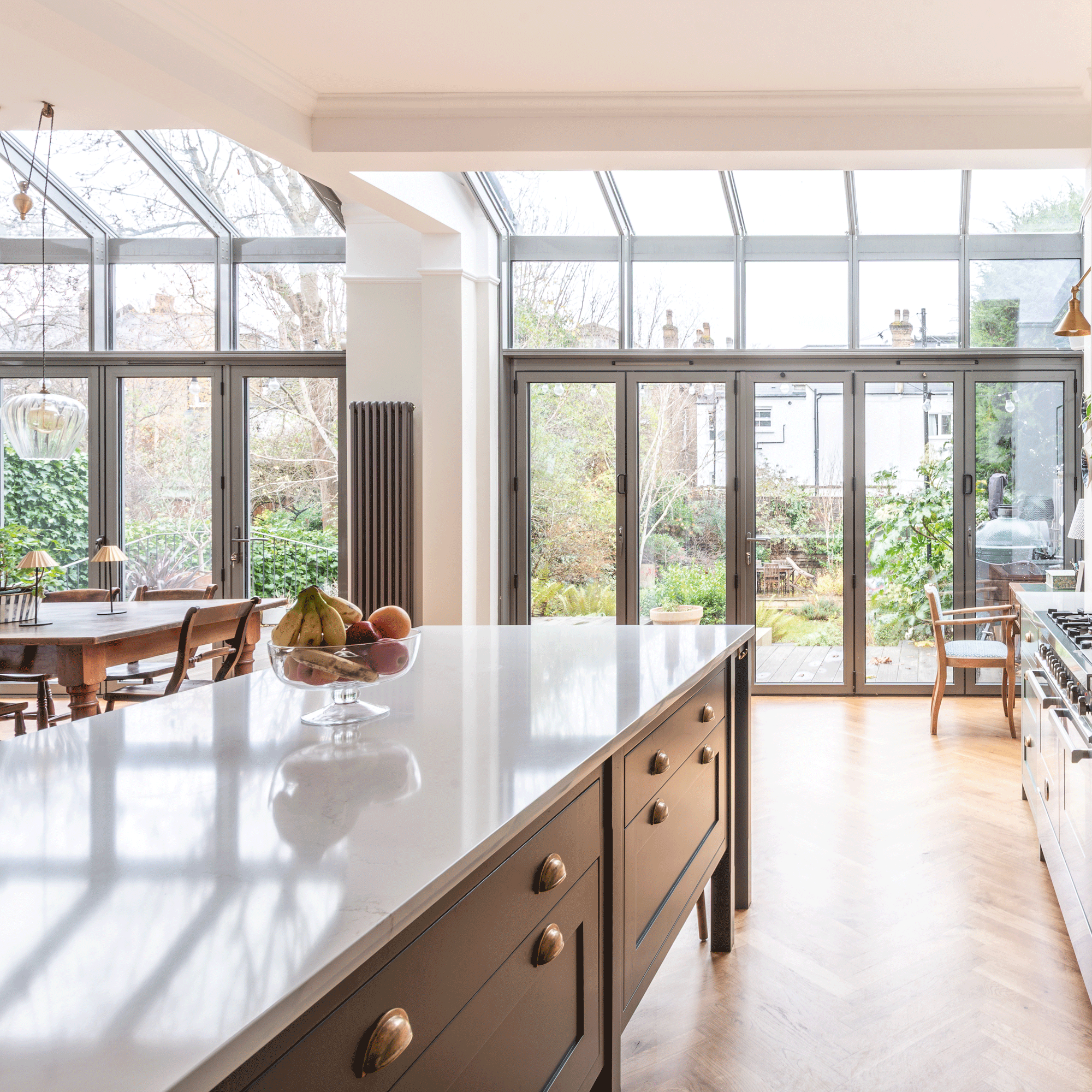 a kitchen diner with timber herringbone flooring and a large kitchen island and a dining table with a view out into a garden with large glass patio doors