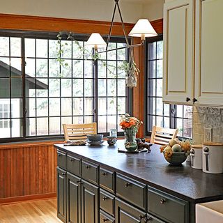 A kitchen with green cabinetry, wooden floors, and a large window