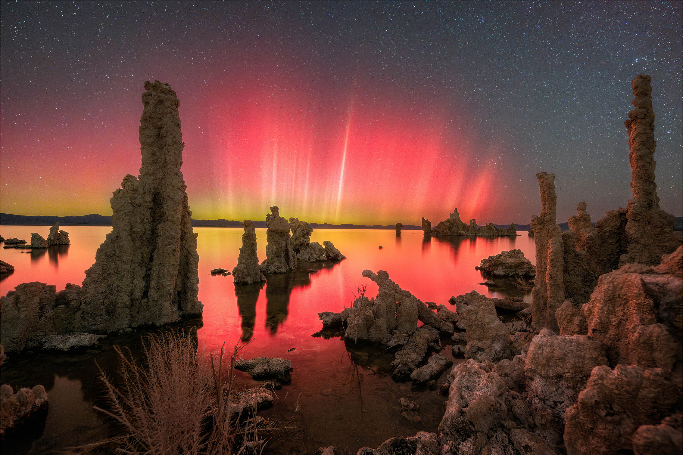 A stunning twilight scene featuring dramatic red auroras reflecting on water, surrounded by unique rock formations under a starry sky