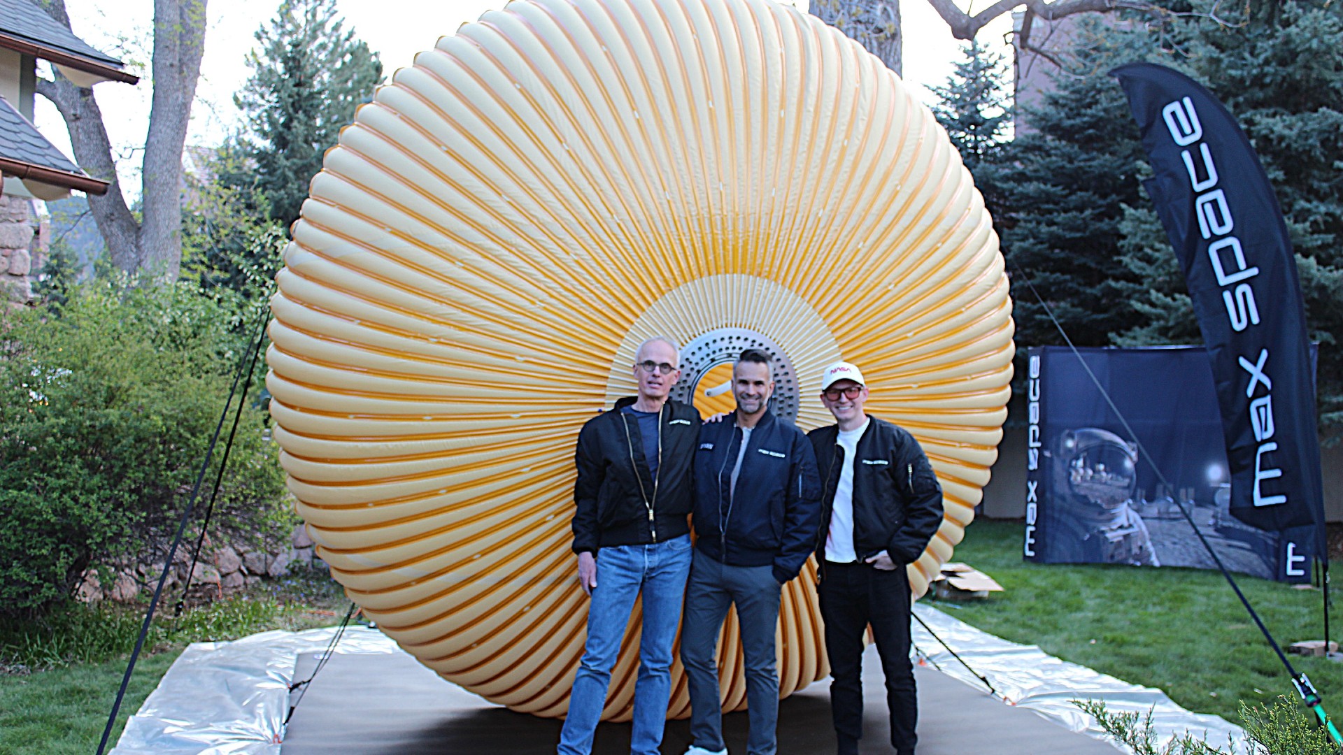 three people in jeans and blazers stand in front of a round crenellated structure in a field