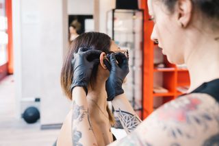 Tattooist piercing ear of customer in parlour - stock photo