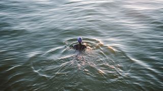 Woman swimming in hat and wetsuit in the sea at sunset
