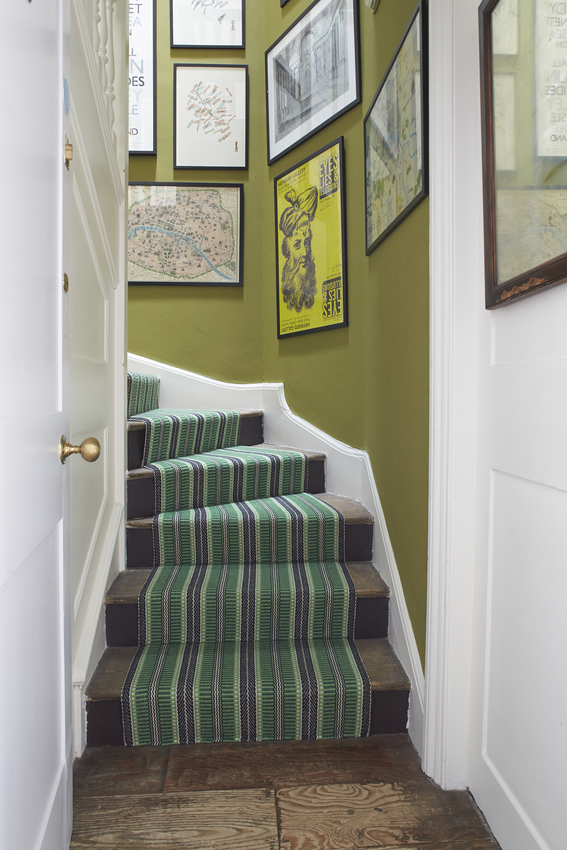 Striped green runner up loft conversion stairs, next to a green wall with artwork on it