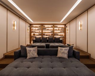 A cinema room with beige walls, low lighting, bookshelf and blue daybeds