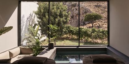 A sumptuous hotel indoor pool features floor-to-ceiling windows overlooking bathing in sunshine, raw Mediterranean nature.