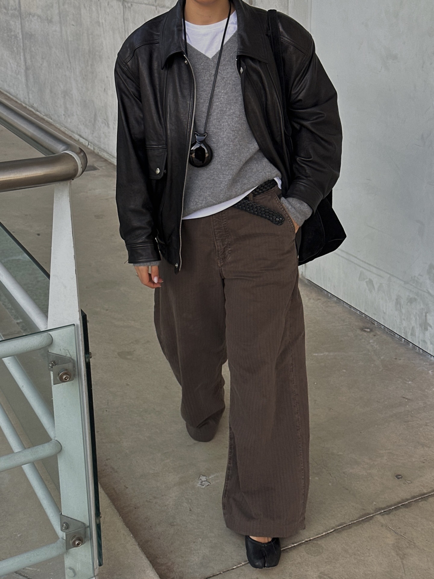 Fashion person Debora Rosa shows what to wear in February. She wears a white t-shirt, grey v-neck jumper, brown trousers, a black leather jacket and black Maison Margiela Tabi's. This image was taken from her Instagram recently.