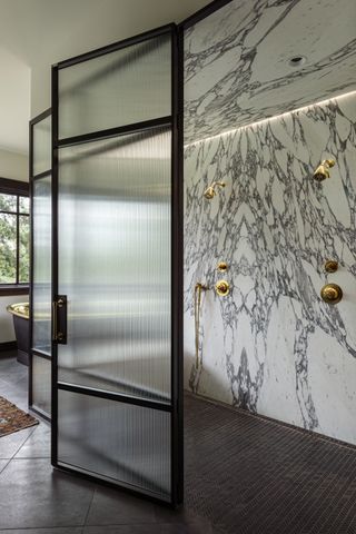 A walk-in shower with a book-matched marble wall, brass hardware, and a fluted shower door