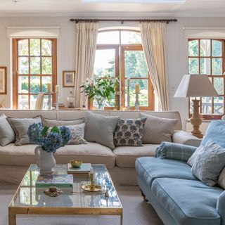 Living room with neutral and blue sofas and wooden french doors leading to garden