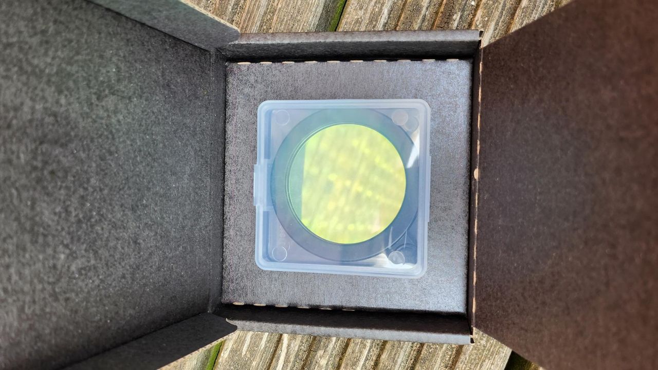 The Vaonis light pollution filter for the Vaonis Vespera Observation Station. It's a green circle with a black outline. It's currently packaged in a square brown box.