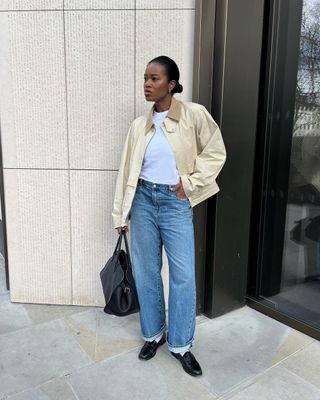 @nlmarliyn wears a cream canvas jacket with a twill collar with blue jeans and black loafers