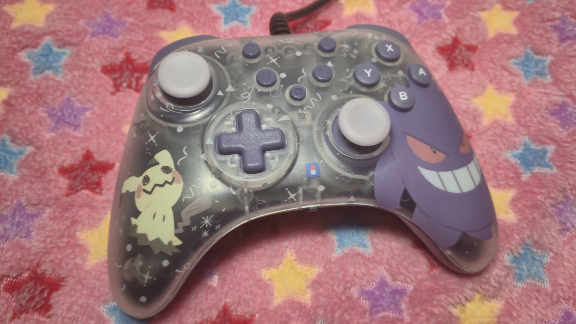 Photo of the Hori Gengar and Mimikyu controller sitting on a pink star patterned blanket.