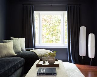 Cozy black living room with white floor lantern lamps, black curtains, black sofa, cream cushions, cream rug, dark wood flooring