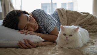 Woman sleeping in bed while her cat lies down next to her