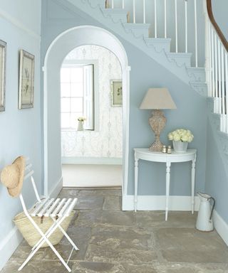 Staircase paint ideas by Little Greene using light blue paint, white chair and console table in hallway with silver picture frame wall decor, flowers and beige lampshade lighting decor