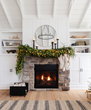 A cottage fireplace with an asymmetrical full garland, candlesticks, and stockings