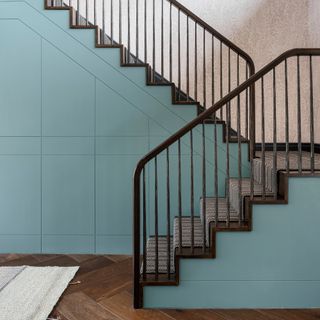 A staircase with black railing, a patterned runner and a teal-coloured built-in storage underneath