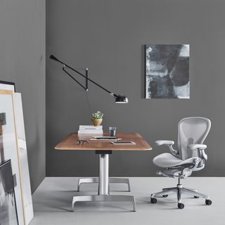A modern, ergonomic, gray mesh office chair. It's photographed in a lifestyle setting, next to a work desk.