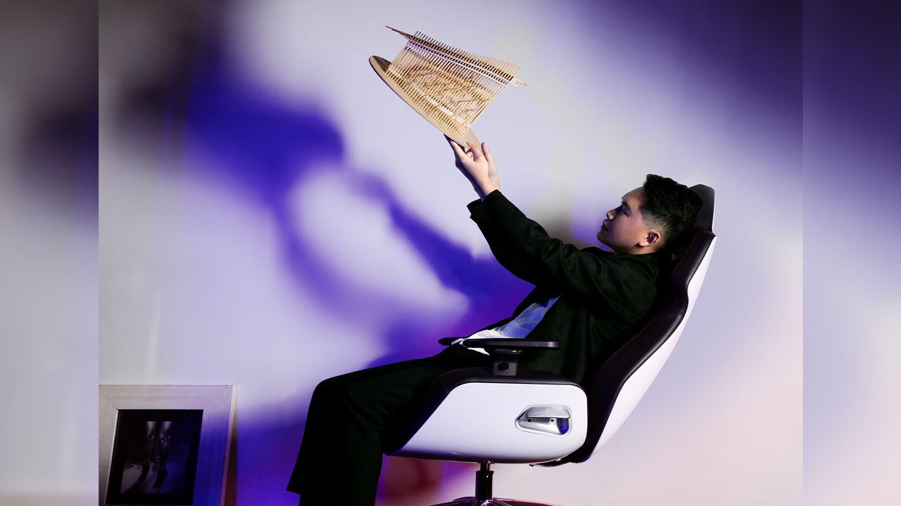 A man holding up an architectural model in a scifi chair.