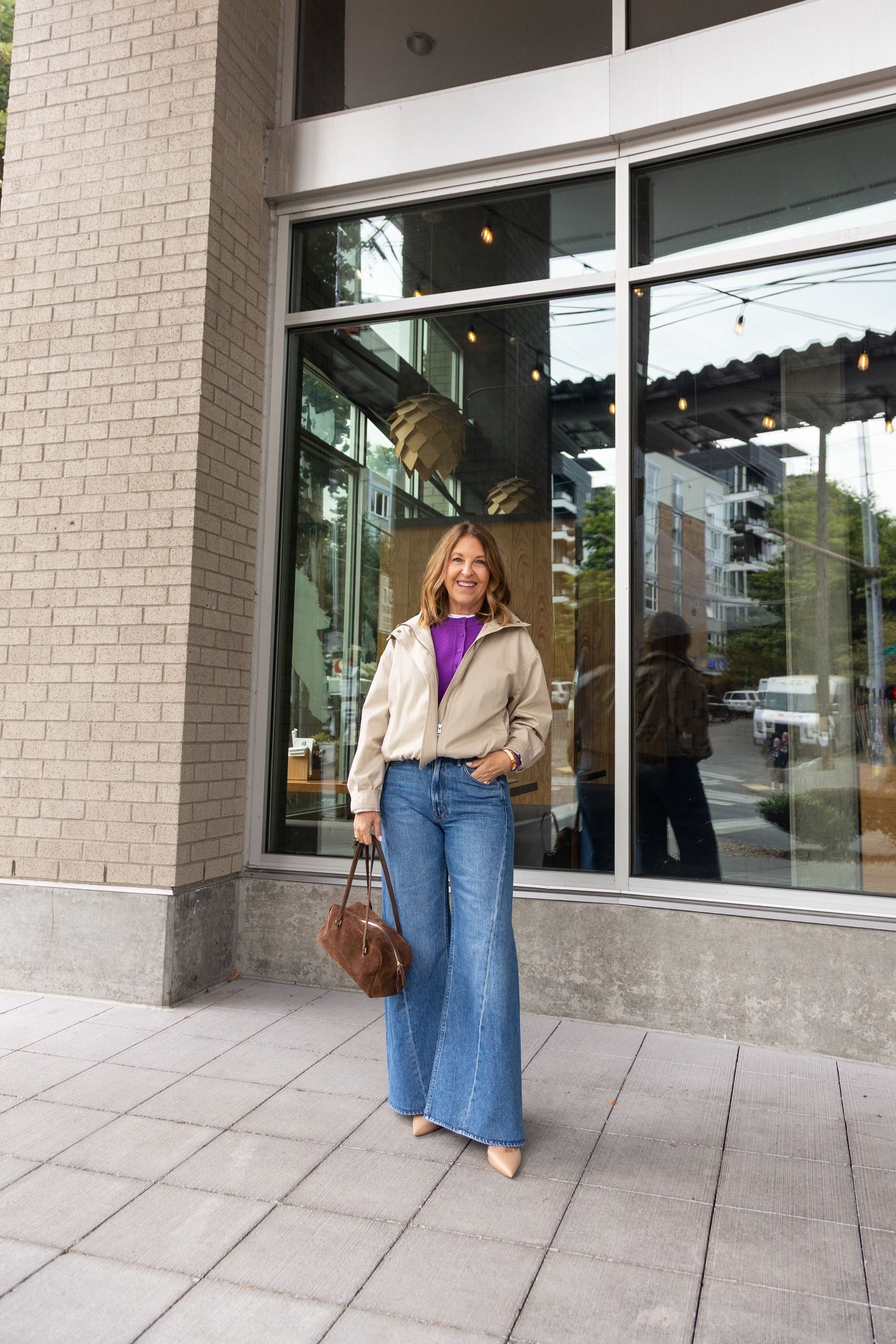 Sandy Koszarek wearing a tan jacket, purple sweater, and jeans.