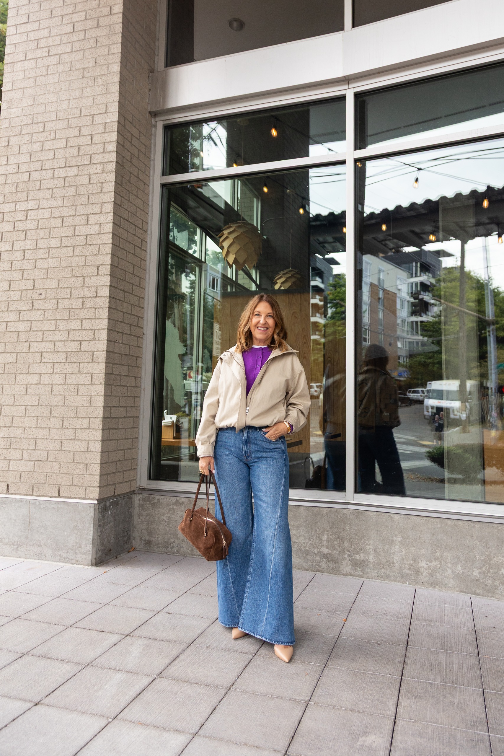 Sandy Koszarek wearing a tan jacket, purple sweater, and jeans.